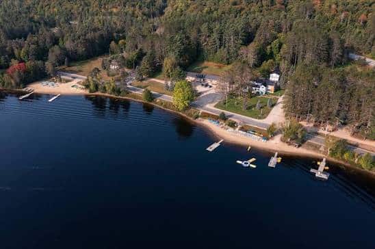 Aerial view of Blue Spruce Resort’s lakeside cottages, beaches and docks on Oxtongue Lake with early fall colour.